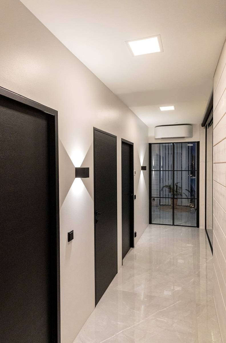 Le couloir est uniformément éclairé par des plafonniers Paneeli 300 et des appliques FUNK noires avec un motif lumineux vert très net en haut et en bas.